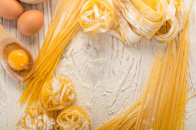 Surowy żółty włoski makaron pappardelle, fettuccine lub tagliatelle z bliska z jajkami. Proces gotowania domowego makaronu jajecznego, długi walcowany makaron, widok z góry niegotowanego spaghetti