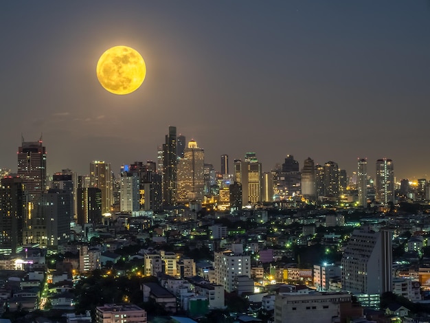 Surrealistyczny widok na panoramę Bangkoku z nieodpowiednią pełnią księżyca na nocnym niebie