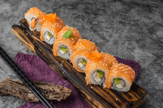 Sushi maki roll z serem, awokado, ogórkiem, sezamem i łososiem na zewnątrz.