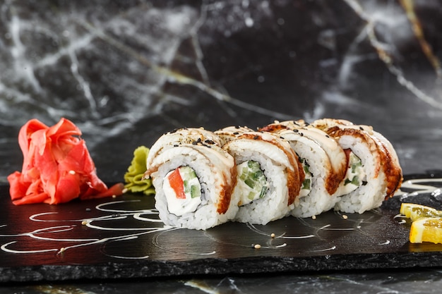 Sushi Rolls z ogórkiem, pomidorem, węgorzem i twarogiem wewnątrz na czarnym łupku na białym tle na czarnym tle z marmuru. Unagi roll Philadelphia. Menu sushi. Poziome zdjęcie.