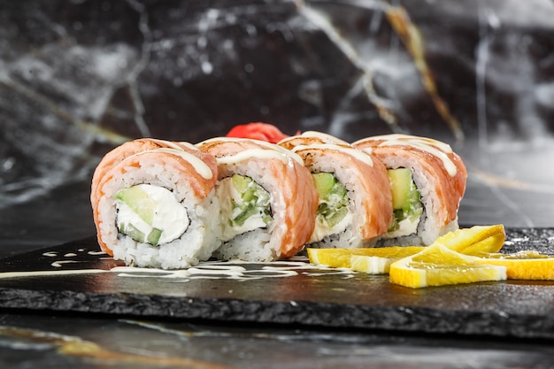 Sushi Rolls z płonącym łososiem, ogórkiem i twarogiem wewnątrz na czarnym łupku na białym tle na czarnym tle z marmuru. Filadelfia roll sushi z ogórkiem. Menu sushi. Poziome zdjęcie.