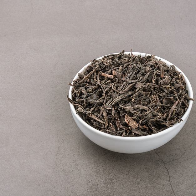 Suszoną herbatę wlewa się do białej ceramicznej filiżanki na szarym tle z teksturą.