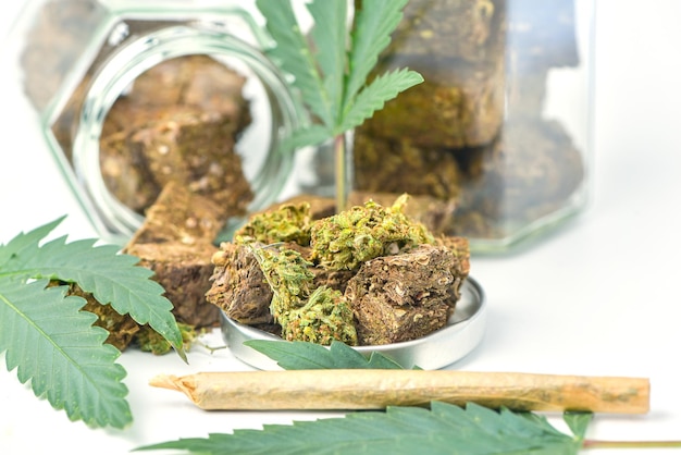 Suszona marihuana w słoiku z zielonymi liśćmi marihuany i rolkami na białym tle Ambulatorium medycznej marihuany Medycyna alternatywna Plantacja konopi dla koncepcji medycznej i biznesowej