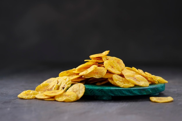 Suszone chipsy bananowe lub wafle bananowerozrzucone na zielonej okrągłej podstawie z izolowanym szarym teksturowanym tłem