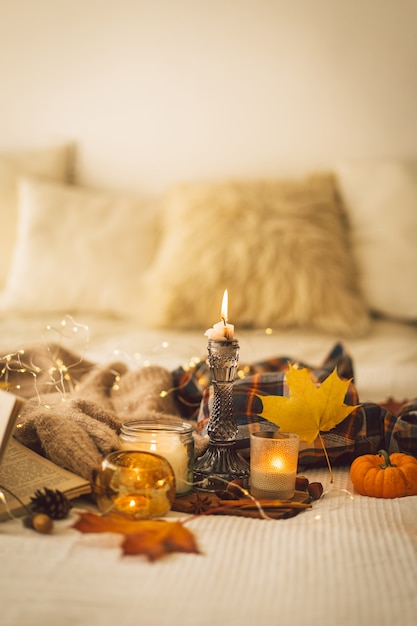 Swetry i świece z jesiennym wystrojem i książką czytają szczegóły martwej natury we wnętrzu domu