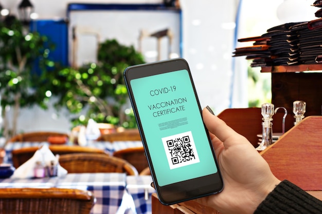 Świadectwo szczepień paszport szczepionki cyfrowa aplikacja szczepionki covid do odwiedzania restauracji i miejsc publicznych ręka ze smartfonem i kodem qr w kawiarni miejskiej