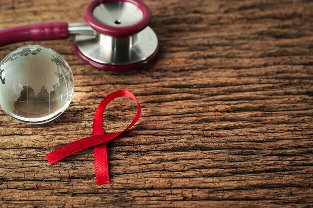 Świadomość Czerwonej Wstążki I Stetoskop Z Pozorowaną Kulą Ziemską Na Drewnianym Tle światowy Dzień Aids Healthcare