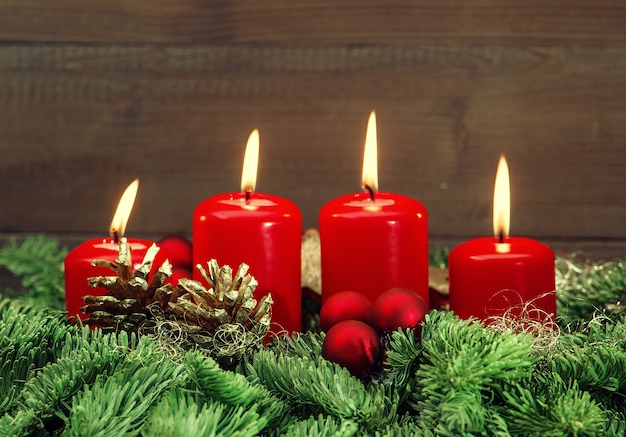 Świąteczna dekoracja adwentowa z czterema płonącymi czerwonymi świeczkami, bombkami i gałązkami choinki. wakacje w tle