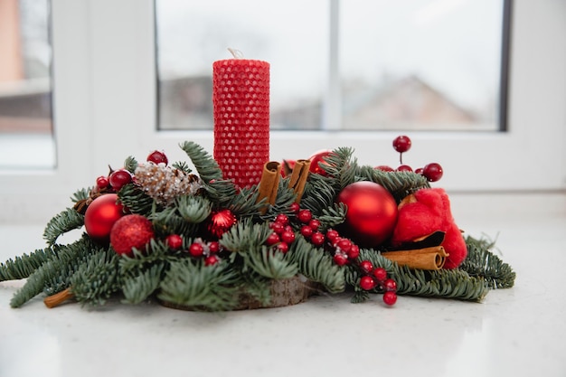 Zdjęcie Świąteczna dekoracja z czerwoną świeczką świerkowe gałązki czerwone kulki szyszki i jagody na parapecie