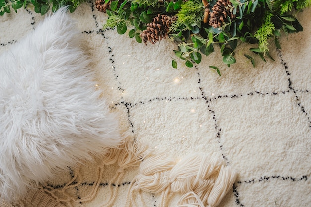 Świąteczna girlanda jodłowa z szyszkami i eukaliptusem na puszystym białym dywanie i futrzanej poduszce.