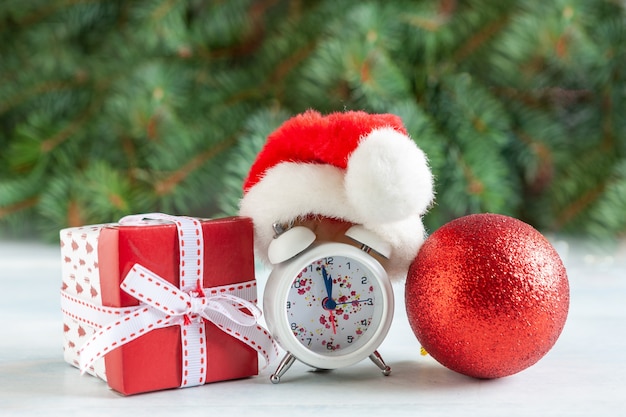 Świąteczna i noworoczna kompozycja z zegarem w czapce Mikołaja przedstawiająca wigilię święta, gałęzie jodły, dekoracje świąteczne i prezenty