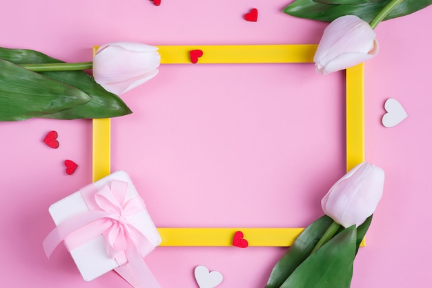 Świąteczna karta zaproszenie z ramą, kwiat świeżych tulipanów i pudełko z papieru czerpanego na pastelowym różowym tle.