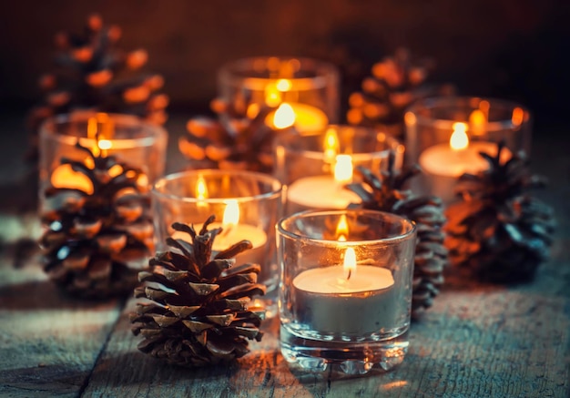 Świąteczna kartka świąteczna ze świecącą małą świeczką i szyszkami jodły na starym drewnianym tle ciemny stonowany obraz w wiejskim stylu selektywnej ostrości