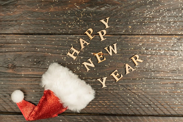 Zdjęcie Świąteczna kartka z życzeniami na nowy rok z czerwonym santa hat i drewnianym tekstem wysuniętym z niego na stole kopiuj psal na tekst koncepcja wakacje