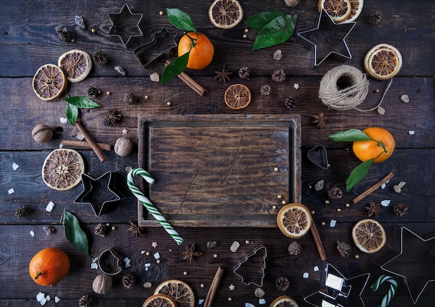 Świąteczna lub noworoczna dekoracja trzciny cukrowej mandarynki suche pomarańcze orzechy włoskie cukrowe i foremki do ciastek w kształcie gwiazdy na ciemnym rustykalnym drewnianym tle Przestrzeń kopii widok z góry