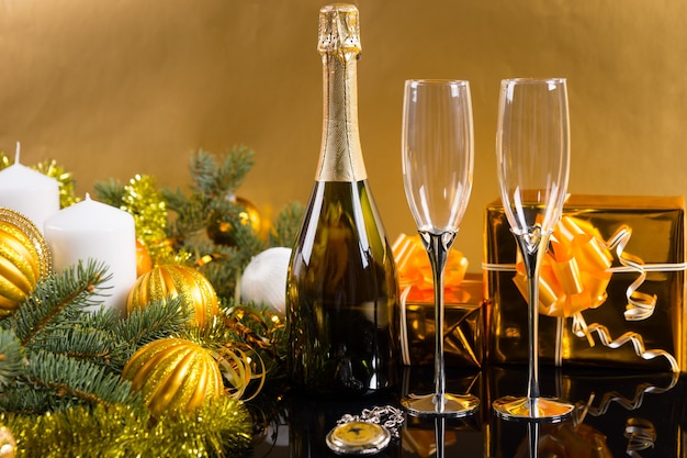 Świąteczna martwa natura - antyczny zegarek kieszonkowy z butelką szampana i kieliszkami na złotym tle z prezentami, świecami i wiecznie zielonymi ozdobionymi bombkami i świecidełkami
