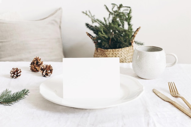 Świąteczna świąteczna zima nakrycie stołu Złote sztućce świerk gałąź lniany obrus porcelanowy talerz obiadowy filiżanka kawy i jedwabne szyszki na białym tle stołu Makieta pusta karta