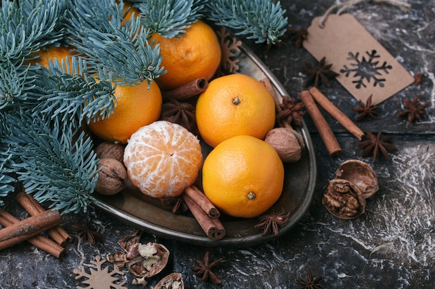Zdjęcie Świąteczna treść, mandarynki, orzech, cynamon, kardamon, metalowe naczynie, świerkowa gałąź, ciemnobrązowe tło, widok z góry