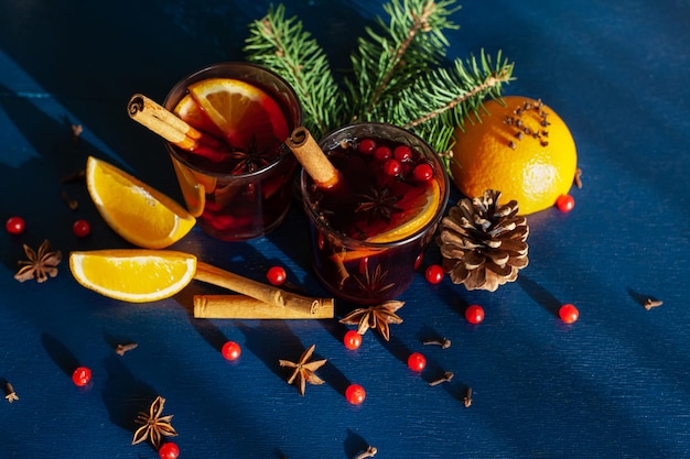 Zdjęcie Świąteczne grzane wino z cynamonem, pomarańczą, anyżem i goździkami z cieniami od promieni słonecznych na niebieskim tle. ferie.