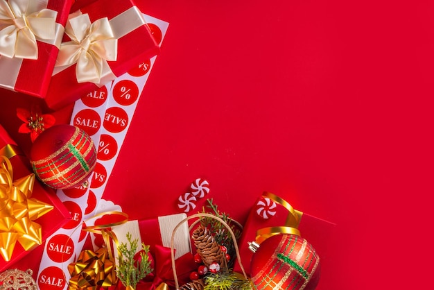 Świąteczne i noworoczne wyprzedaże zakupy tło baner szablon Jasnoczerwony płaski leży z papierową torbą zakupową pełną prezentów ozdoby świąteczne gałęzie drzewa jęczmienia z zakupami i etykietami sprzedaży