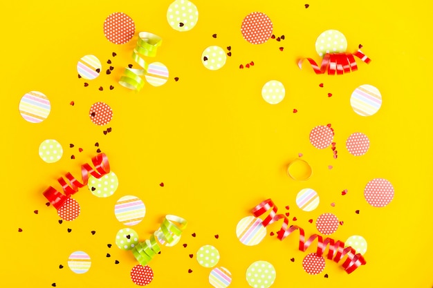 Świąteczne konfetti, wstążki i brokat na jasnym żółtym tle