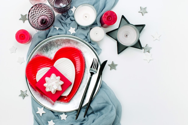 Świąteczne nakrycie stołu. Białe i czerwone naczynia w formie serca, szklanki do napojów, świece i sztućce na białym tle. Walentynki lub koncepcja ślubu
