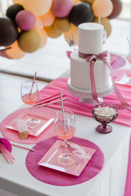 Świąteczne nakrycie stołu w różowych kolorach, białe talerze, szklanki do napojów. Ozdoba kolorowe balony. Baby shower, urodziny lub impreza dla dziewcząt.
