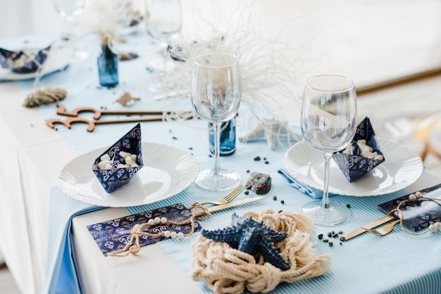 Świąteczne nakrycie stołu w stylu morskim. Eleganckie talerze, papierowe kubki, słomki, niebieski materiał. Papierowe łodzie z pianką. Koncepcja chłopiec urodziny lub prysznic.