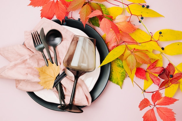 Świąteczne nakrycie stołu z jasnymi jesiennymi liśćmi na pastelowym tle.