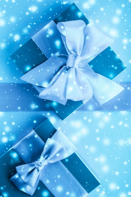 Świąteczne prezenty i świecący śnieg na zamarzniętym niebieskim tle Prezenty świąteczne niespodzianka