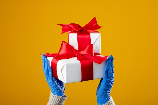 Świąteczne prezenty świąteczne covid mierzy kobiece dłonie w ochronnych rękawiczkach trzymające pudełka z prezentami zaklejone taśmą