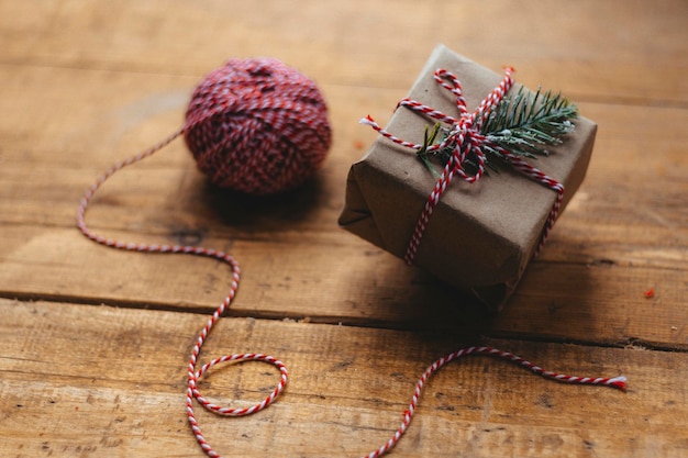 Świąteczne pudełko przewiązane biało-czerwoną wstążką na drewnianym, rustykalnym stole obok sznurka do pakowania Pakowanie świątecznych prezentów