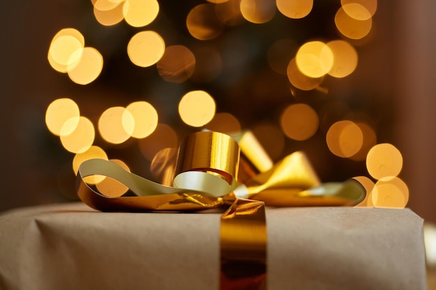 Świąteczne pudełko ze złotą wstążką na świątecznym oświetlonym tle drzewa nowego roku Święta Bożego Narodzenia