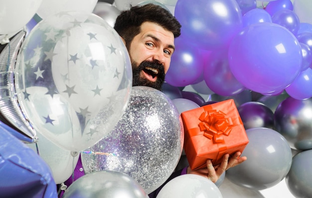 Świąteczne wydarzenie lub przyjęcie urodzinowe szczęśliwy człowiek z balonami z helem trzyma brodatego mężczyznę w pudełku