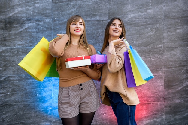 Świąteczne Zakupy. Dwie Szczęśliwe Kobiety Z Kolorowymi Torebkami Na Prezenty Pozują Po Zakupach