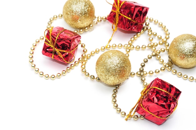 Świąteczne złote bombki i prezenty w czerwonym opakowaniu przewiązane łańcuszkiem na odosobnionym białym tle