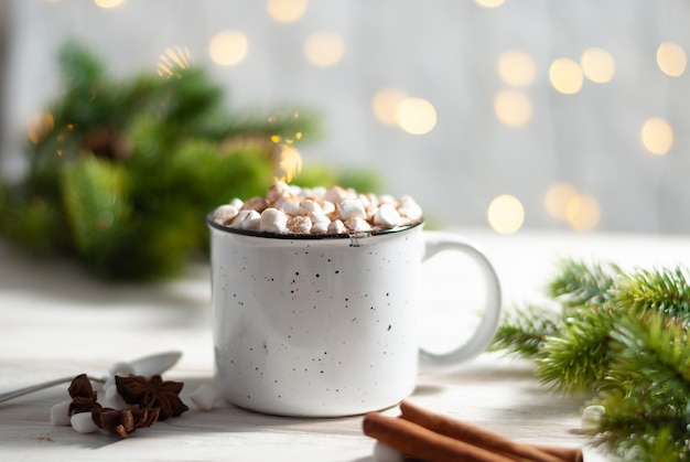 Świąteczny biały kubek z gorącą czekoladą i piankami na tle cynamonu i jodły