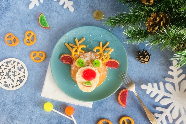 Świąteczny jadalny jeleń z bułeczek i marmolady na niebieskim talerzu na świątecznym stole obok cukierków