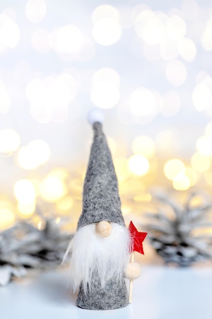 Świąteczny krasnal ze świątecznymi dekoracjami na tle ośnieżonych szyszek jodłowych, pionowe zdjęcie