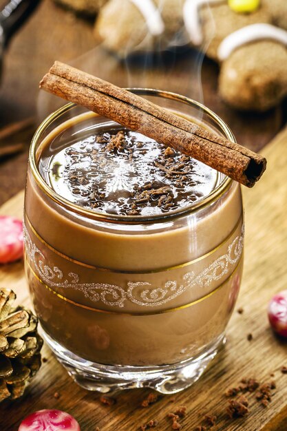 Świąteczny kubek ozdobiony laską cynamonu z gorącą czekoladą i piernikowym ludzikiem w tle