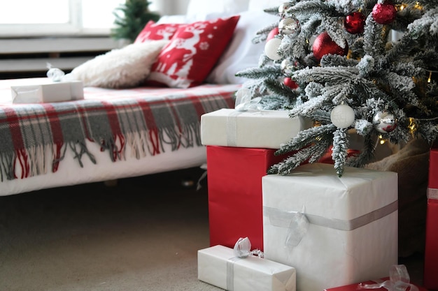 Świąteczny wystrój sypialni Pod oknem podwójne łóżko oraz choinka z prezentami