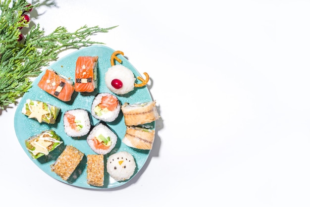 Świąteczny zestaw sushi ze śmiesznie dekorowanymi rolkami w postaci symboli bożonarodzeniowych: mikołaj, jeleń, bałwan, jodła, świąteczne menu sushi baru, świąteczna makieta z dostawą