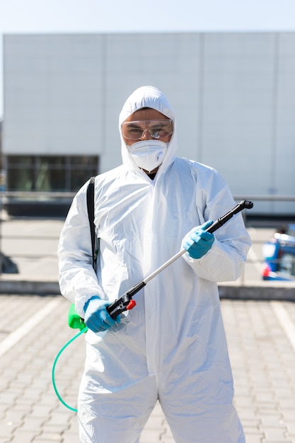 Światowa pandemia. Dezynfektor w kombinezonie ochronnym i masce, przechowujący chemikalia do dezynfekcji na zewnątrz