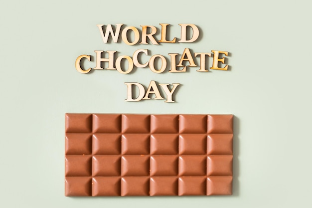 Światowy dzień czekolady tekst z tabliczką czekolady płaski widok z góry na pastelowym zielonym tle