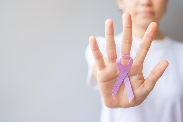 Światowy dzień walki z rakiem (4 lutego). Kobieta ręka trzyma lawendową fioletową wstążkę do wspierania ludzi żyjących i chorych. Opieka zdrowotna i koncepcja medyczna