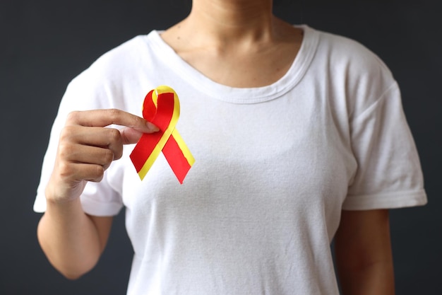 Światowy dzień zapalenia wątroby i świadomość zakażenia wirusem HIV z czerwoną żółtą wstążką w symbolicznej kokardce kobiecej dłoni