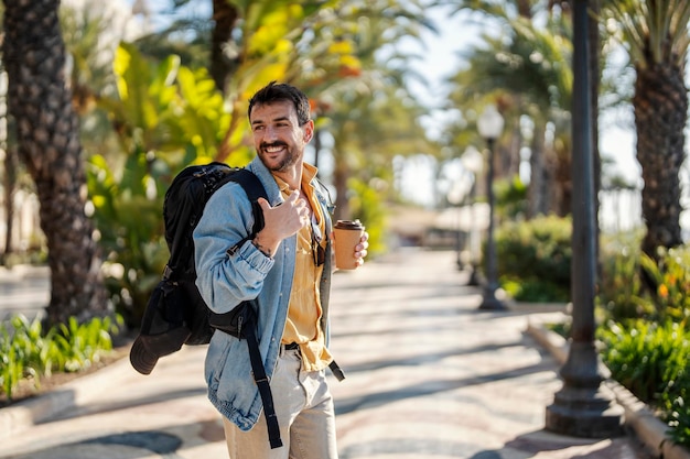 Światowy podróżnik z plecakiem i kawą idzie ulicą podczas wizyty w Hiszpanii