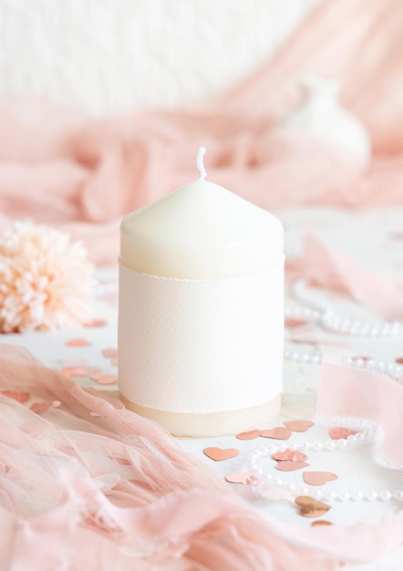 Świeca z pustą etykietą w pobliżu różowej dekoracji serca i tul na białym stole
