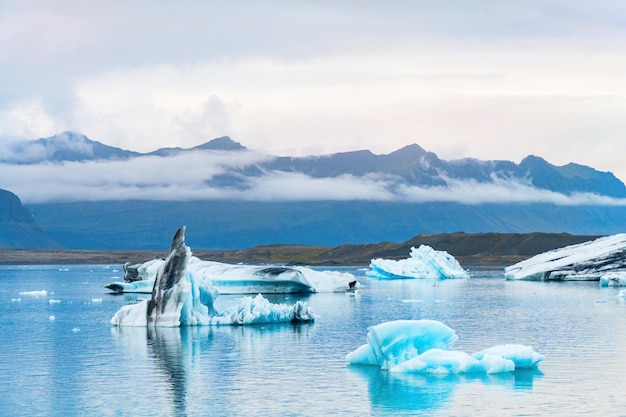 Świecące niebieskie góry lodowe pływające w lagunie lodowcowej Jokulsarlon na tle lodowca górskiego. Południowa Islandia, Park Narodowy Vatnajökull. Skopiuj tło. Miejsce na tekst.