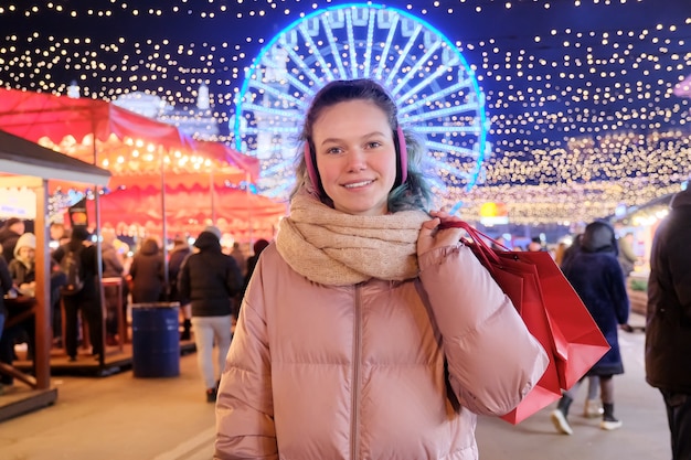 Święta Bożego Narodzenia i Nowego Roku, szczęśliwa nastolatka z czerwonymi torbami na zakupy na jarmarku bożonarodzeniowym